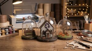 Laser cut Halloween dome scenes on a workbench next to a laser cutter