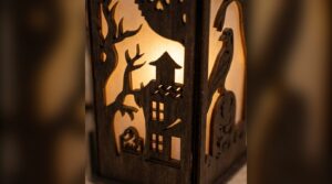 Close-up of a laser cut lantern panel with a haunted house and bare tree silhouette