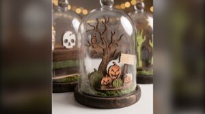 Laser cut pumpkin patch tree scene with an owl under a glass dome, next to a spell books dome and a zombie hands dome